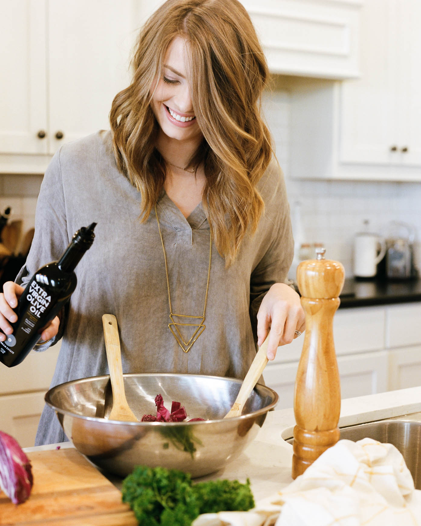 woman in kitchen tossing salad with organic olive oil