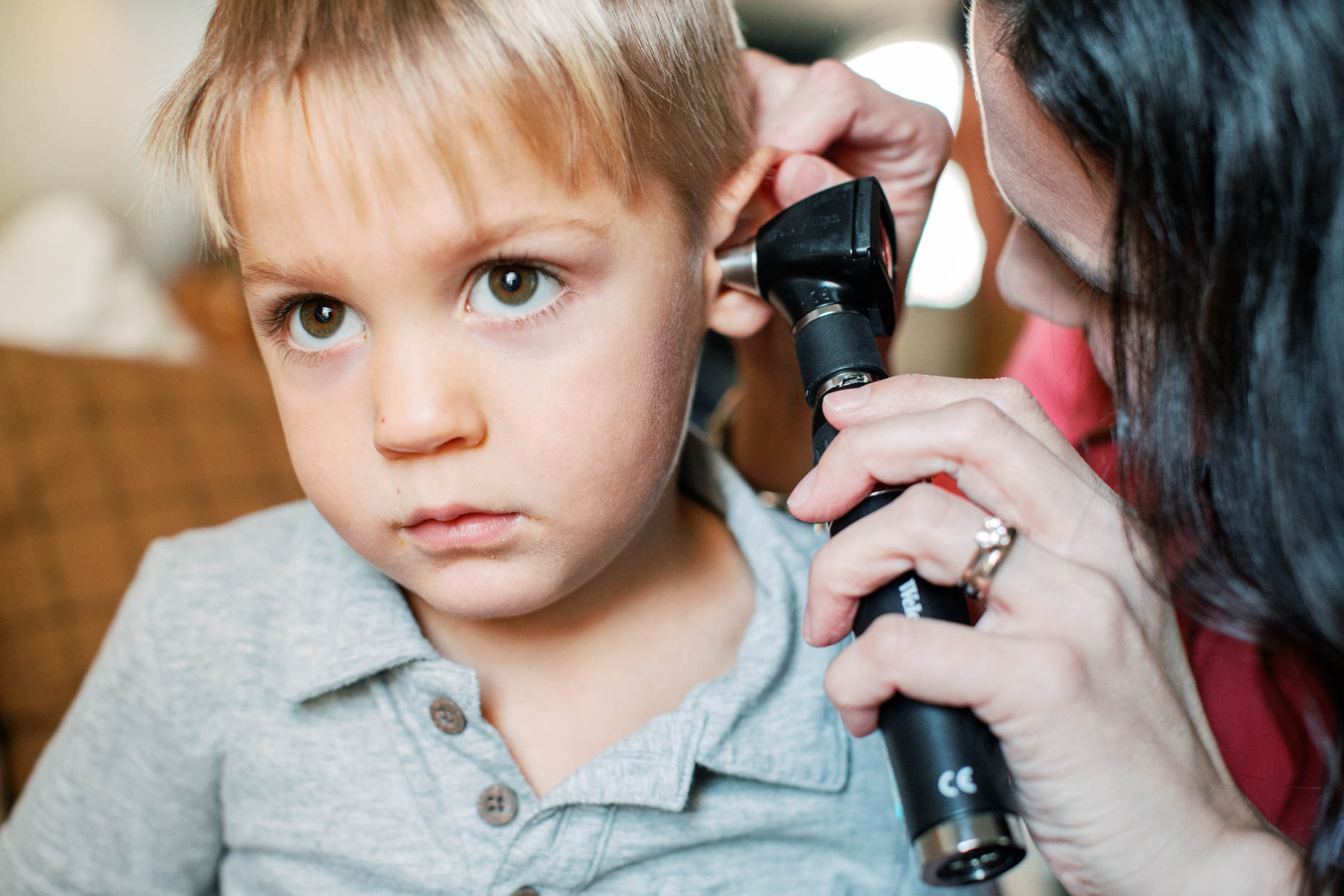 A small boy getting ears examined by a healthcare provider at home