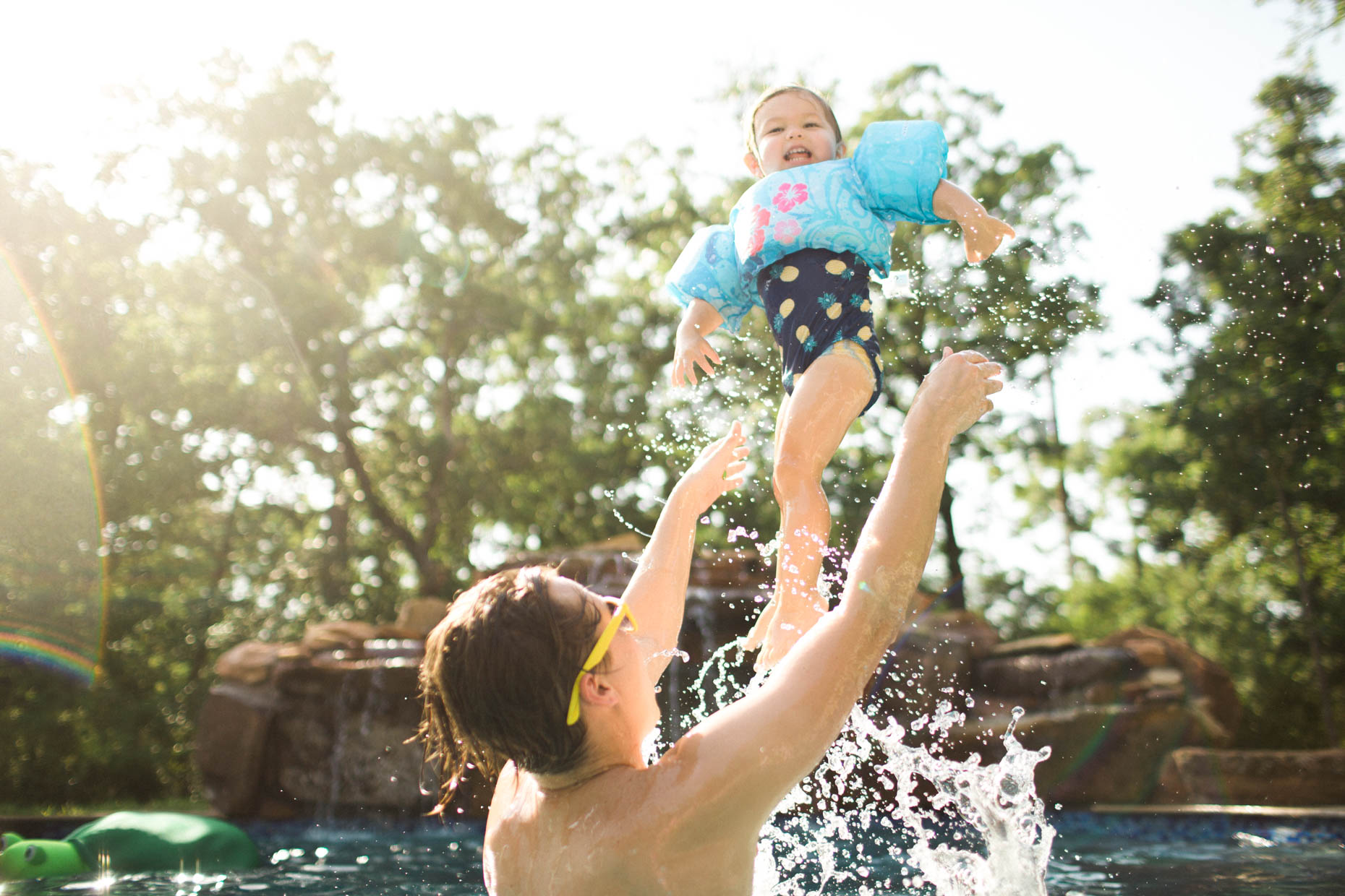 Father tossing baby girl in the air while swimming in a pool. Fun and exciting summertime photo