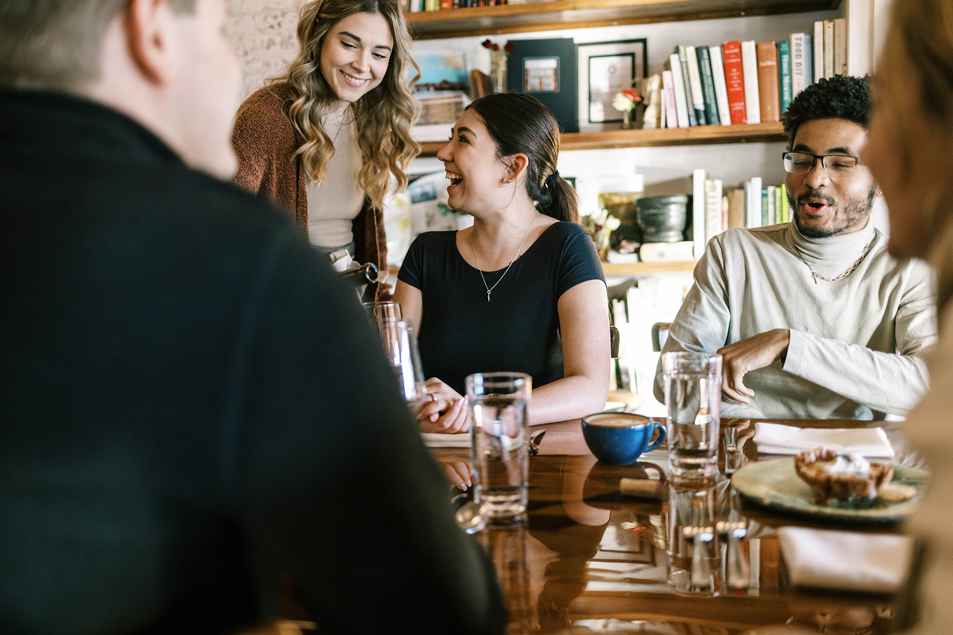 Restaurant experience at high end local restaurant server pouring wine while guests laugh and enjoy meal