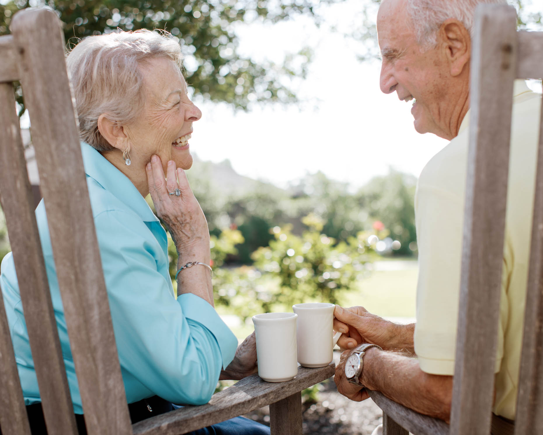 Retired couple enjoying coffee outdoors in rocking chairs at senior living community