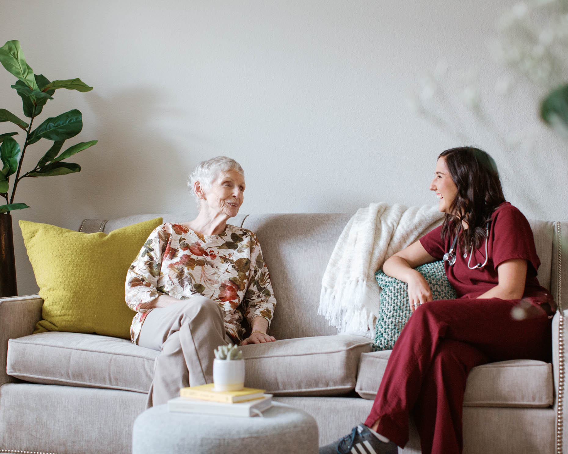 Retired woman sitting on couch with healthcare provider in a senior living community