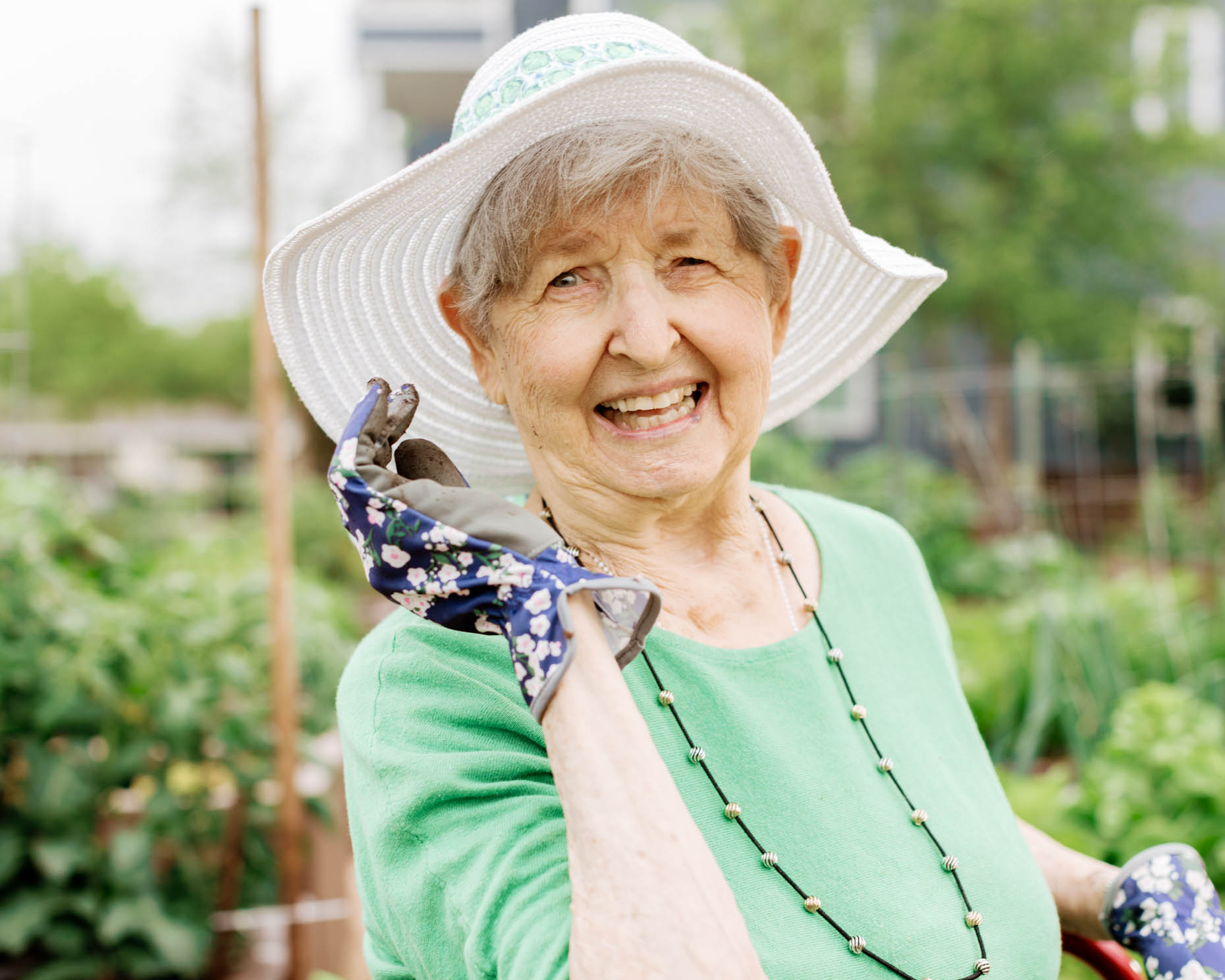 Natural portrait of a retired woman wearing green shirt and garden hat working with plants at a retirement community