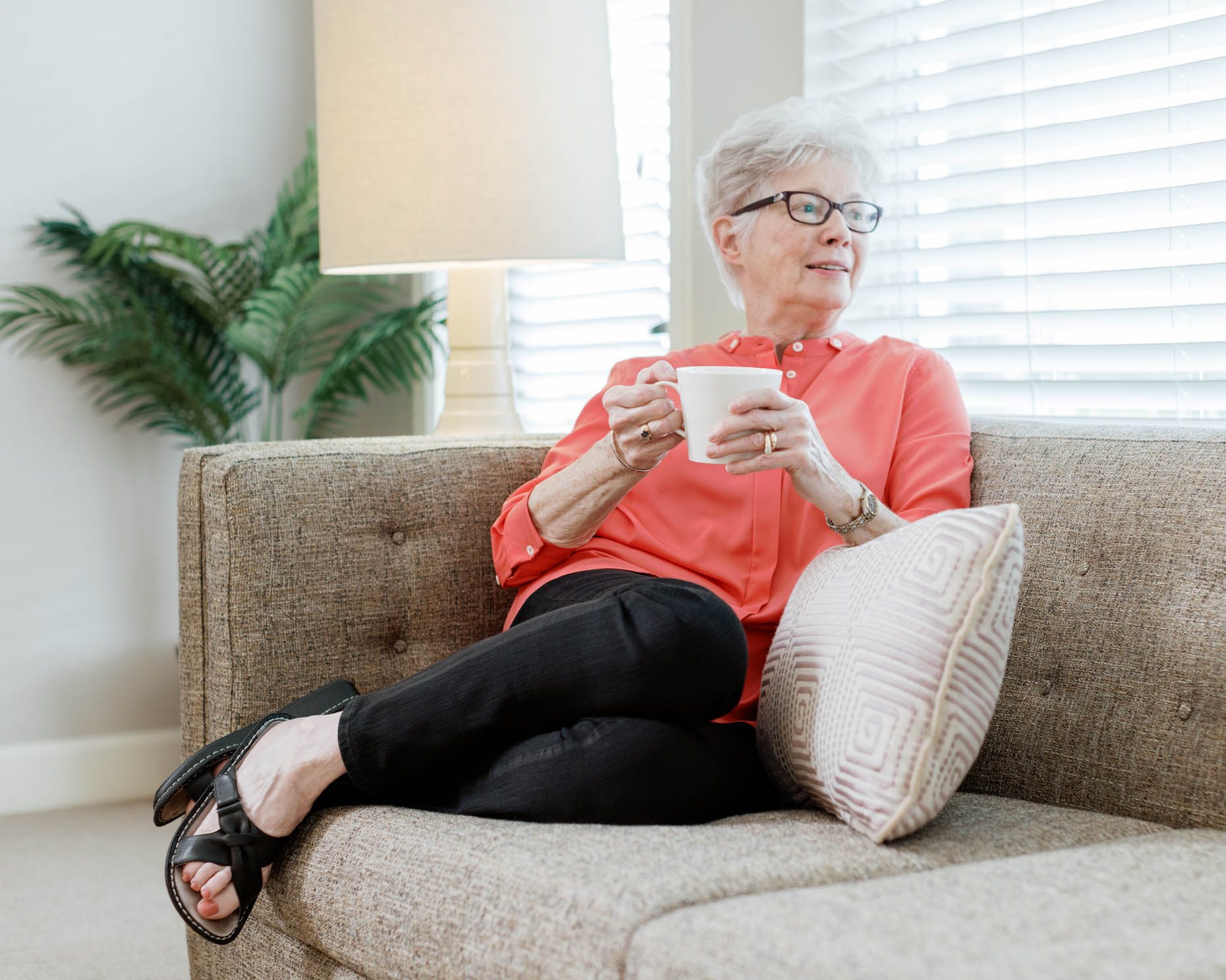 Retired woman sipping coffee while cuddled on couch at a senior living community
