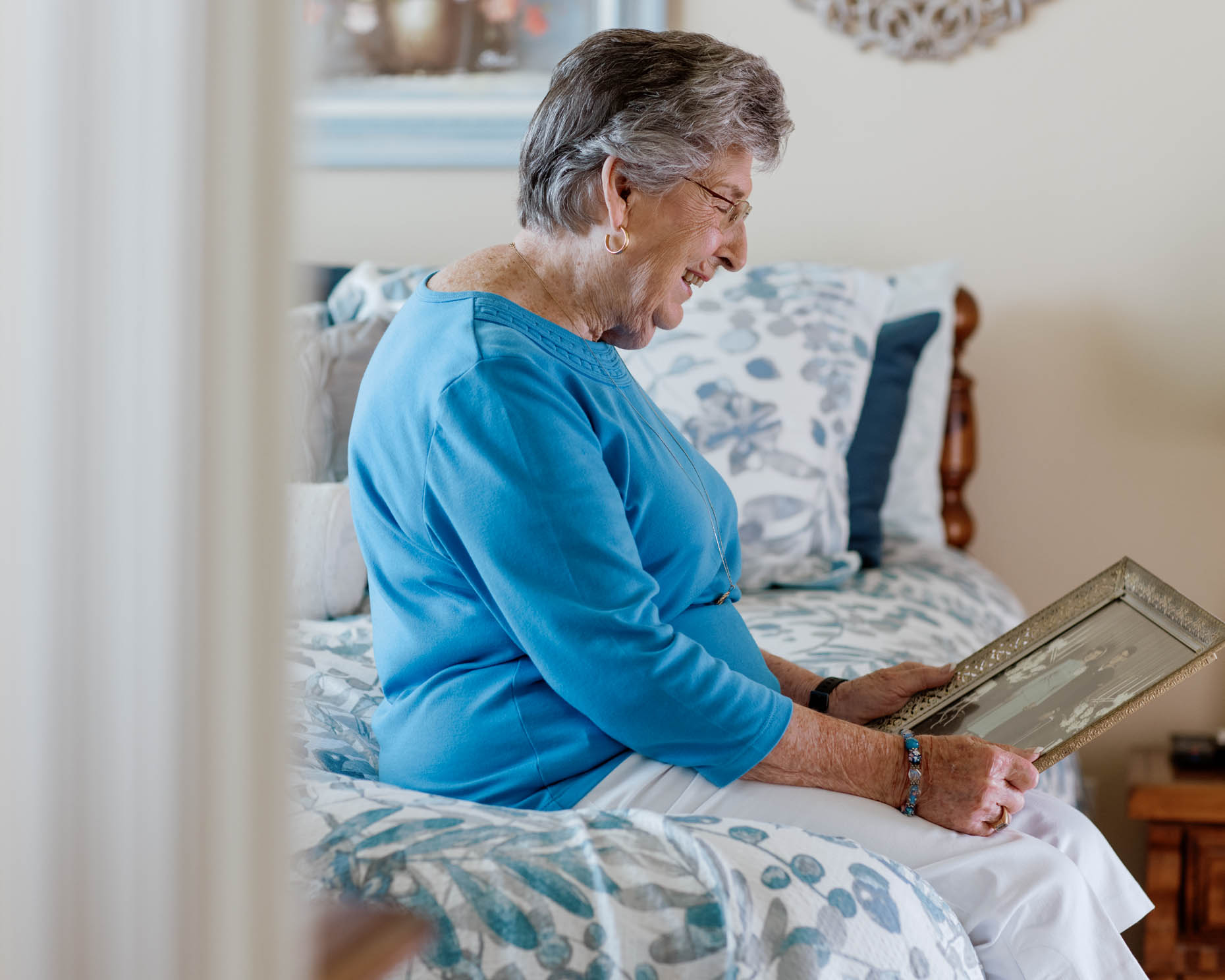 Retired woman sitting on side of bed looking at an old photograph at a senior living community