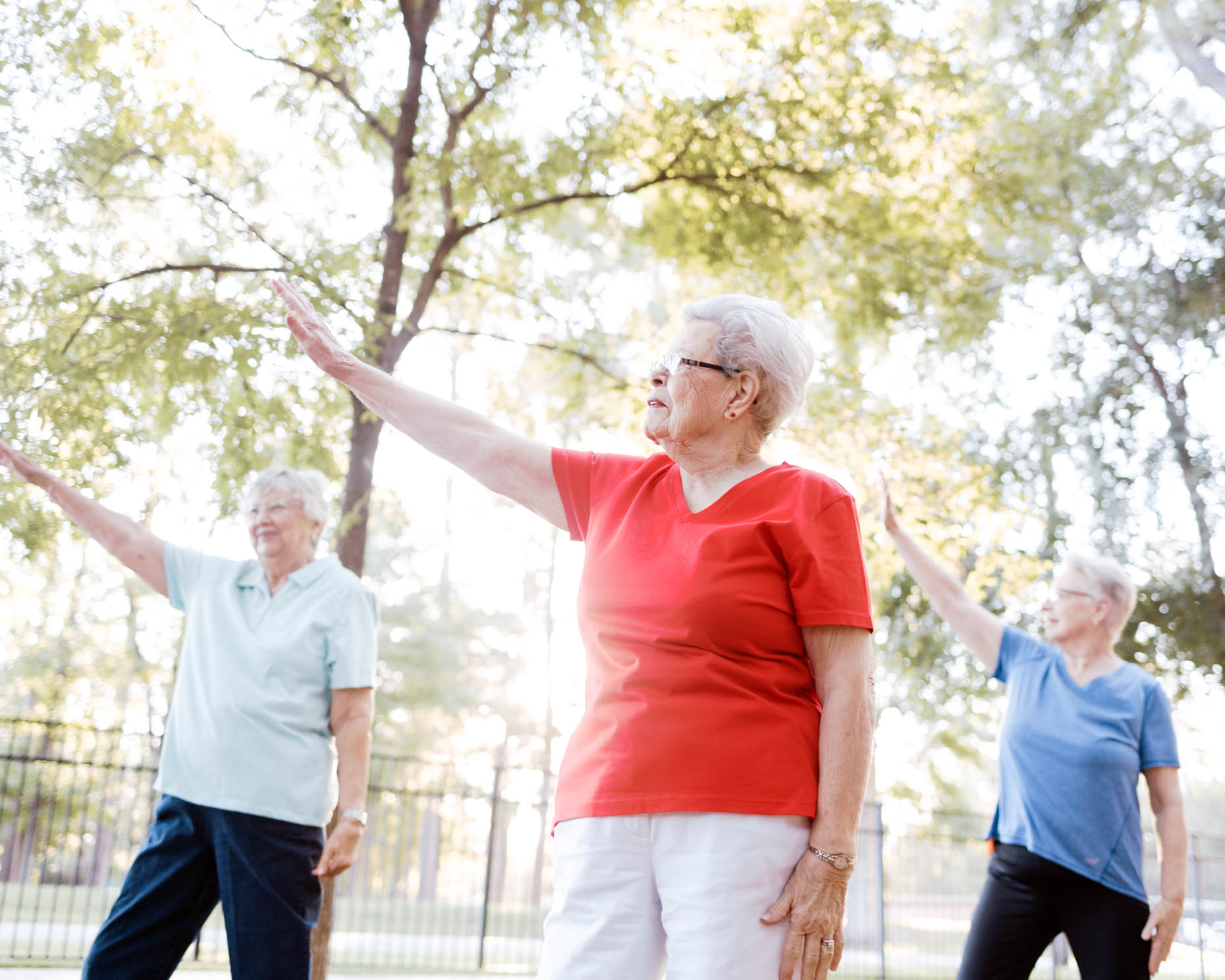 Three retired women doing tai chi workout outdoors in the morning at a senior living community