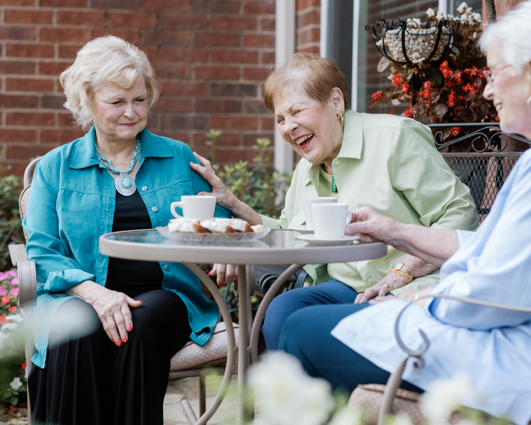 Three retired women laughing at outdoor sitting area at a senior living community