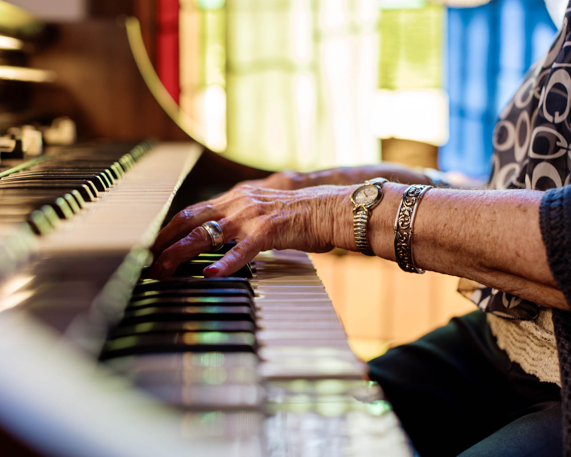 Elderly person playing the organ with a stained glass backdrop at a senior living community
