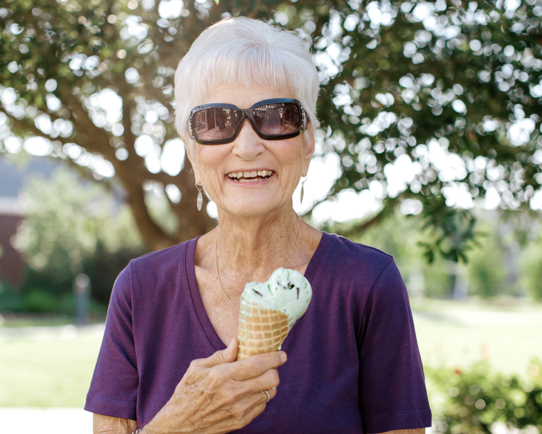 Retired woman in sunglasses eating ice cream cone outdoors at a senior living community