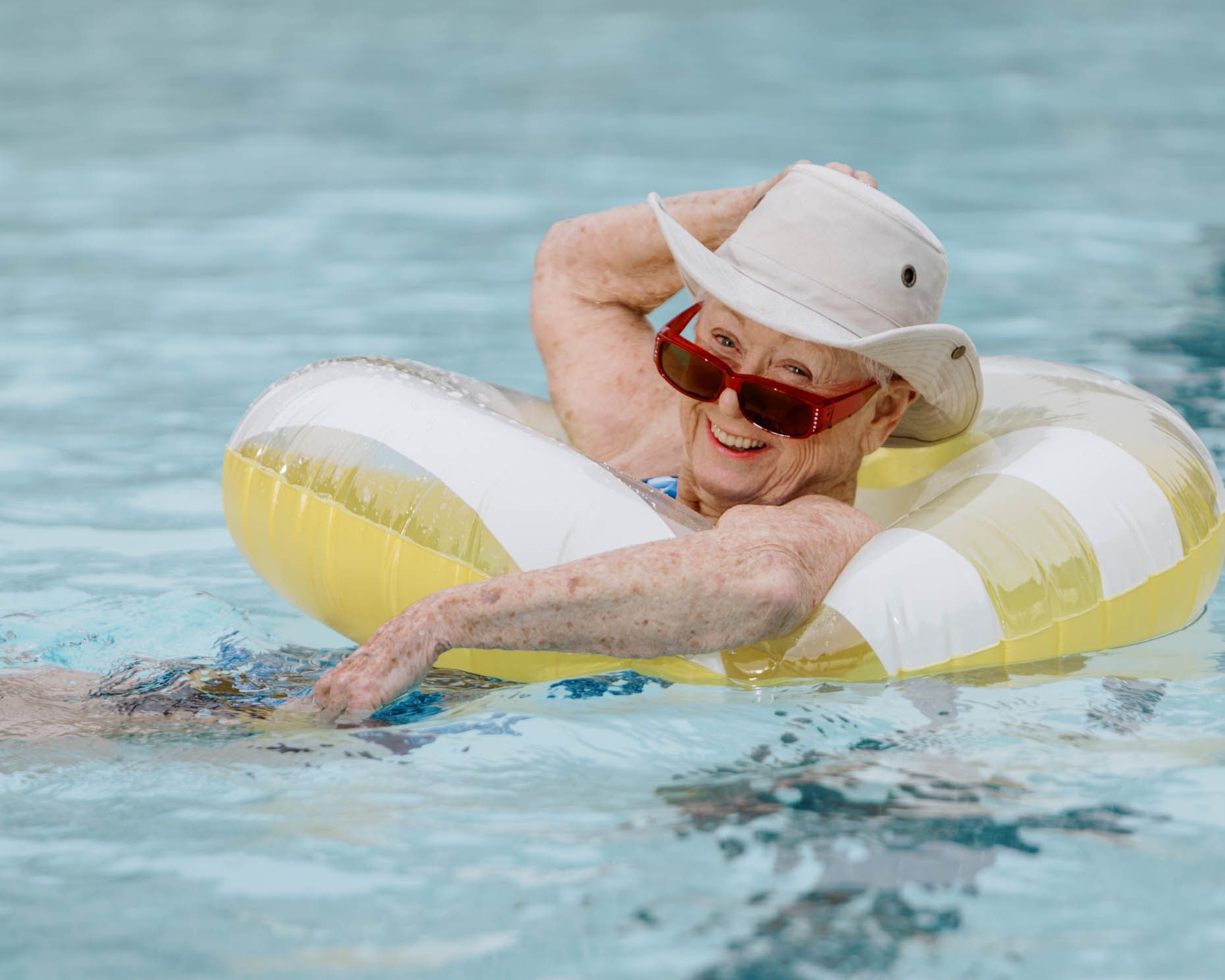 Retired woman in swimming pool with hat on at a senior living community