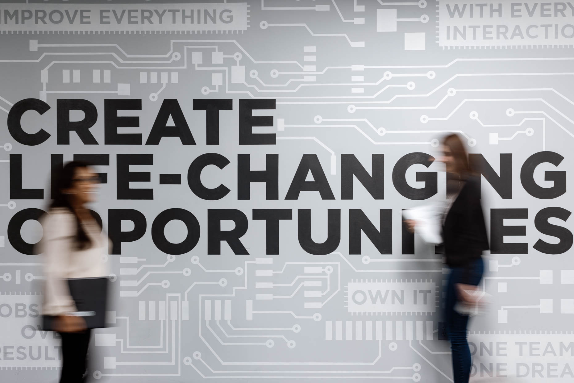 Two women in the workplace walking in front of a graphic mural for a software company