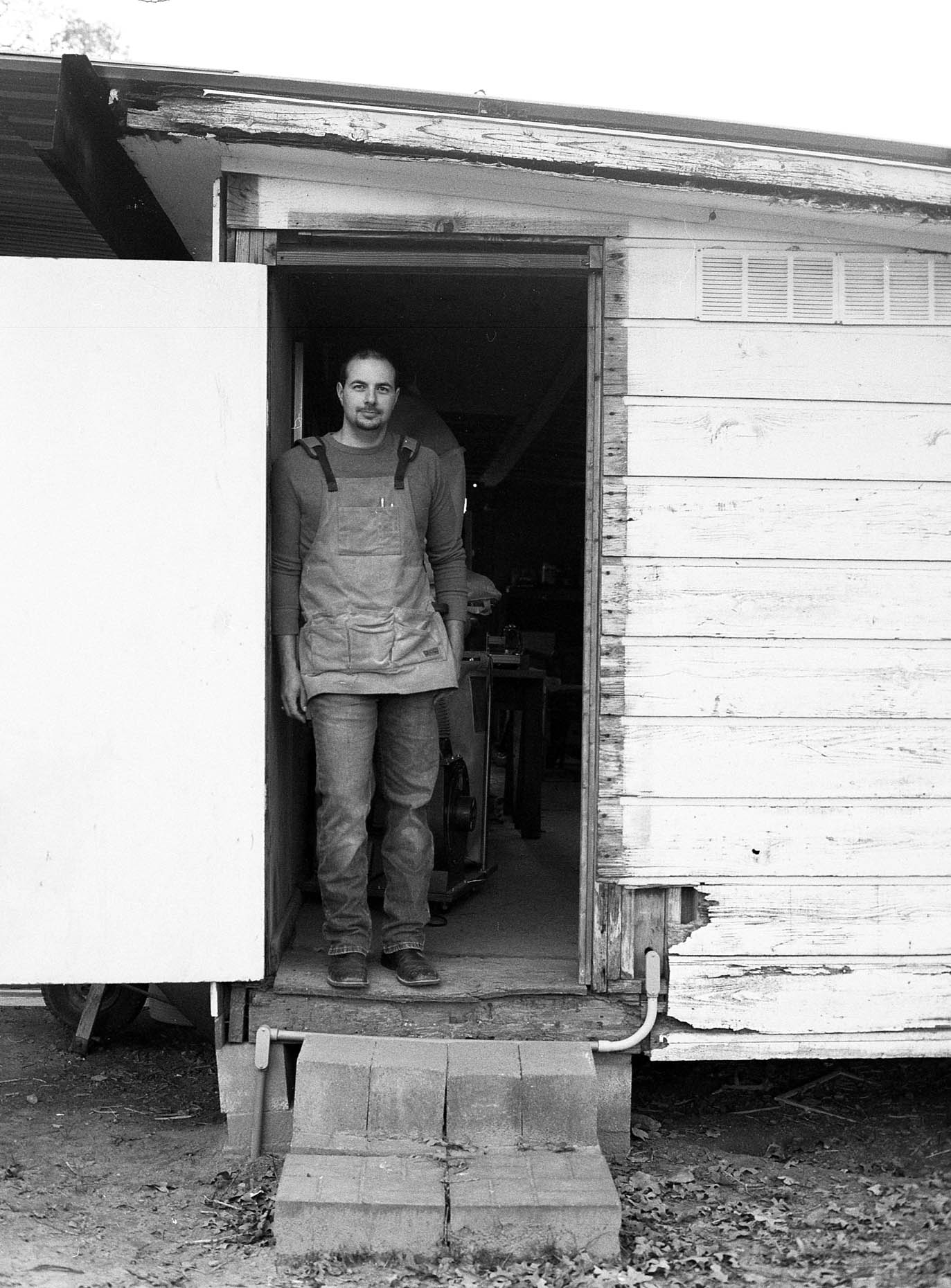 portrait of wood worker standing in doorway of his shop