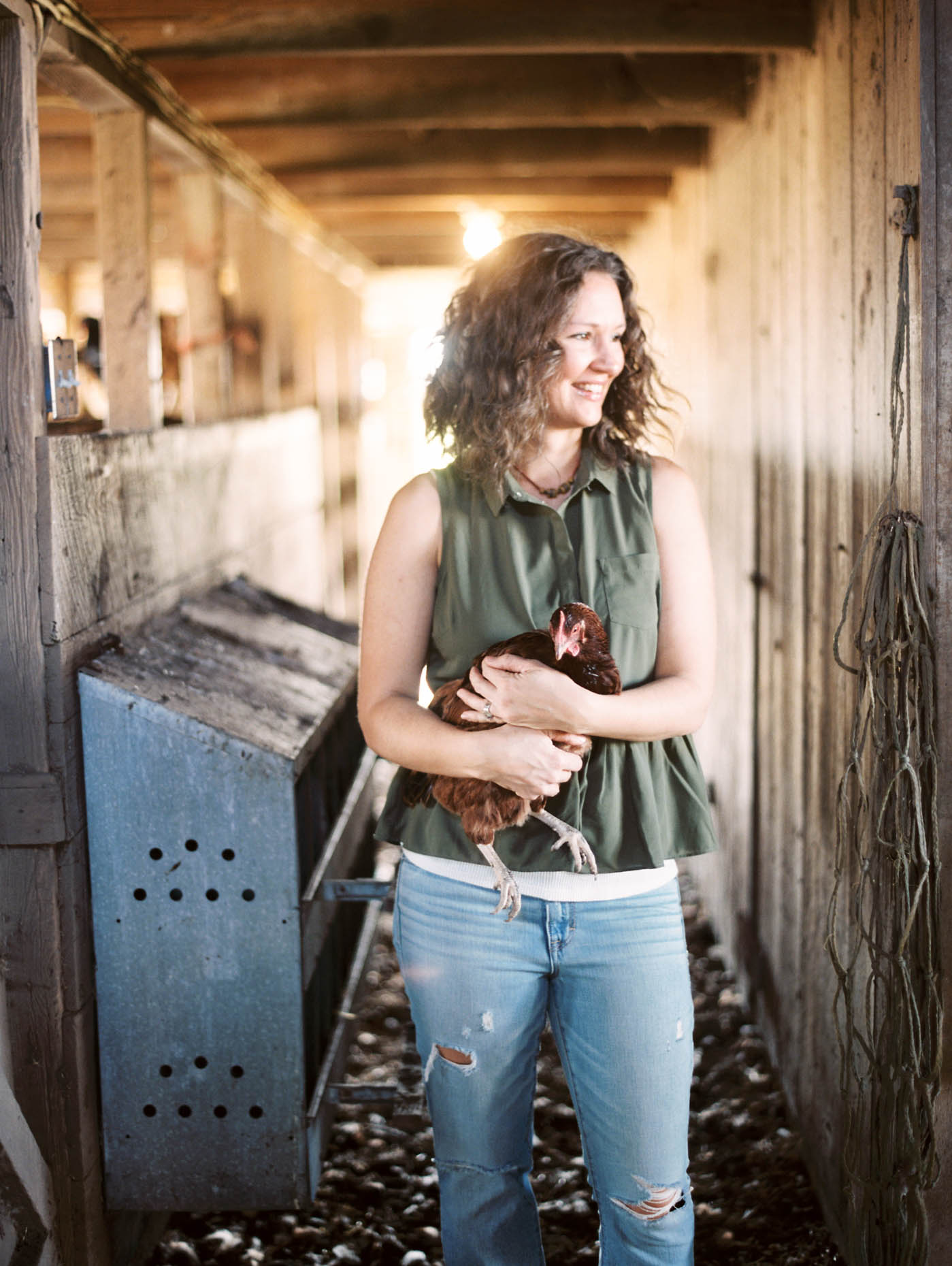 Lifestyle portrait of a female Texas farmer holding a chicken inside of a rustic barn